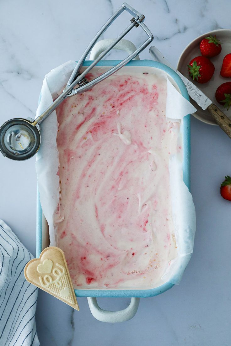 strawberry ice cream in a blue bowl next to some strawberries and other food items