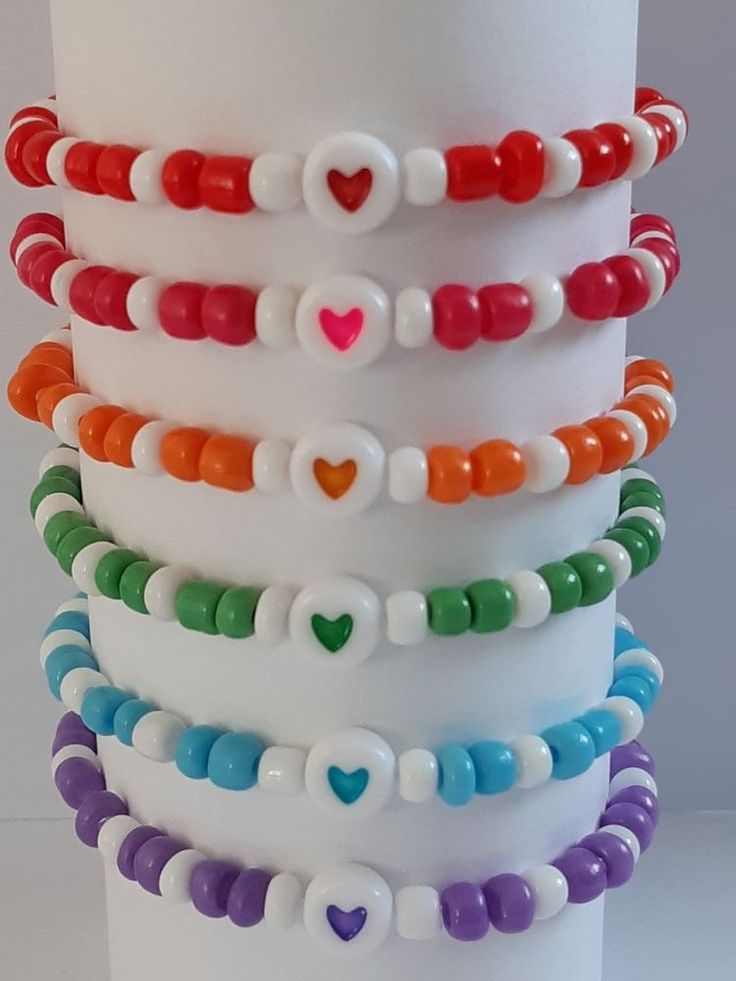 a stack of multicolored bracelets on top of a white pillar with a heart in the middle