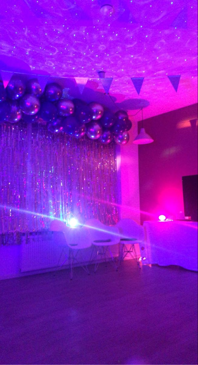 a party room with balloons and streamers on the ceiling is lit by purple lighting