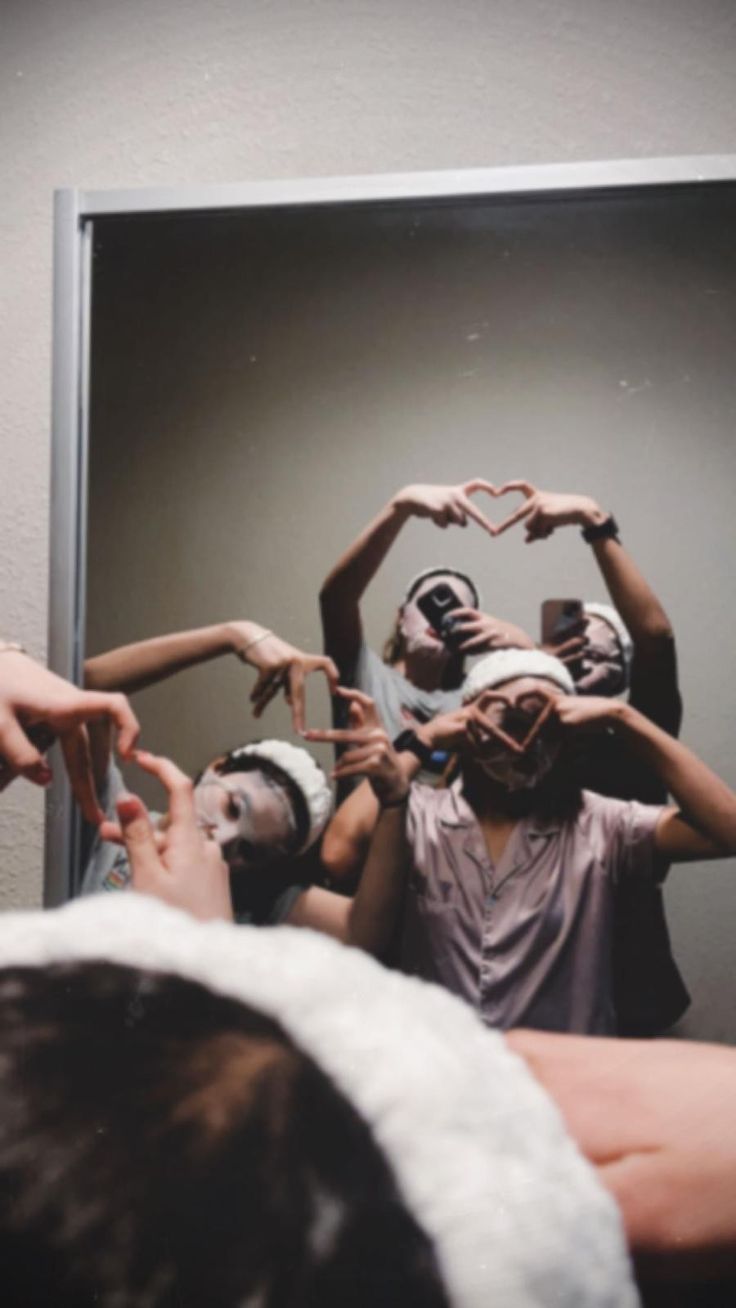 a group of people standing in front of a mirror making heart shapes with their hands