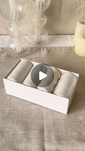 an open box containing two bracelets and a candle on a table with a vase in the background