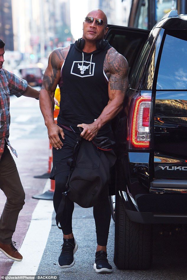 the rock is getting out of his truck and walking down the street with his hand in his pocket