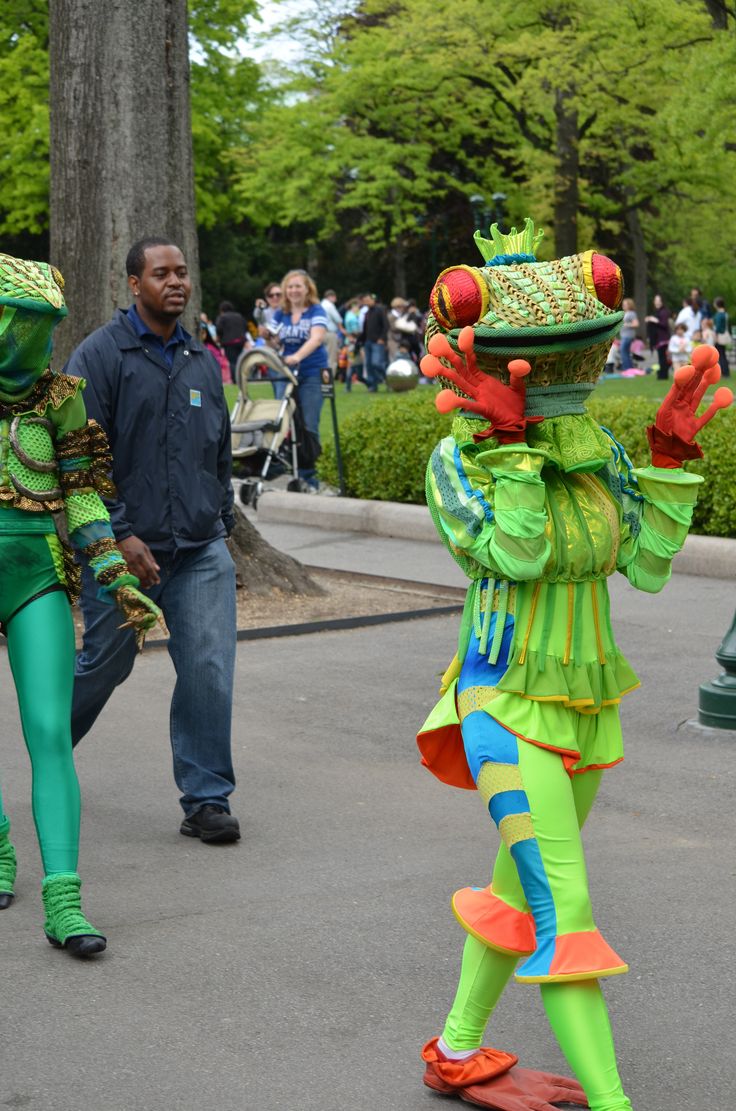 two people dressed in costumes walking down the street with one person wearing green and orange