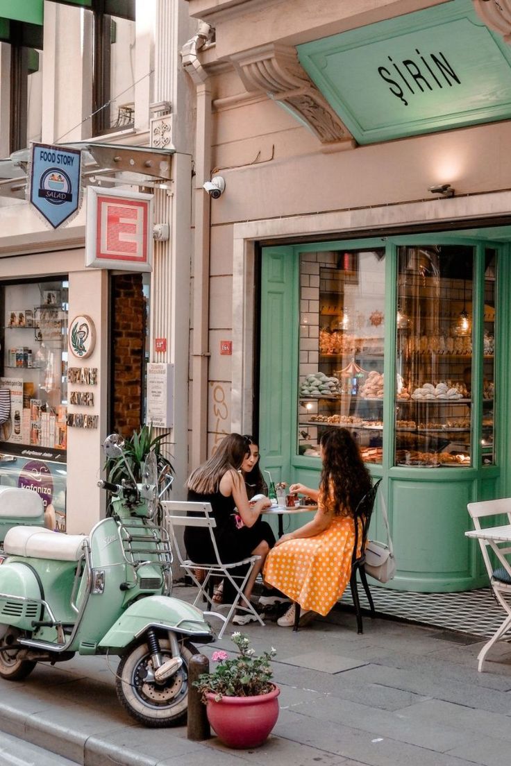 two women sitting on the sidewalk in front of a store with scooters parked outside