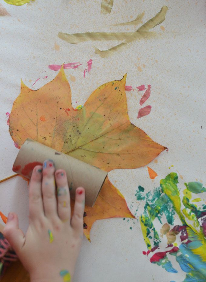 a child's hand on a piece of paper with leaves painted on it