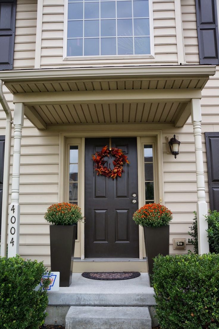 a front door with two planters and a wreath on the side of it in front of a house