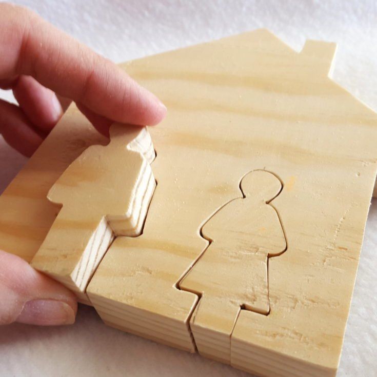 a person holding a piece of wood with a house cut out of it