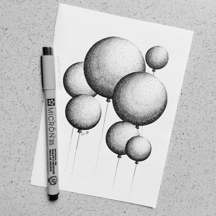 an ink drawing of balloons on paper next to a marker and some pens are laying on the table