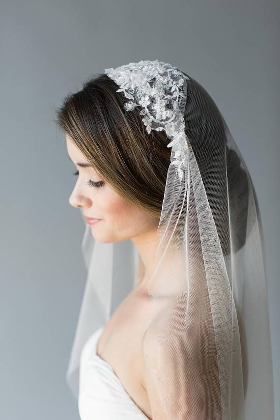 a woman wearing a wedding veil with flowers on the side and hair comb in her hand