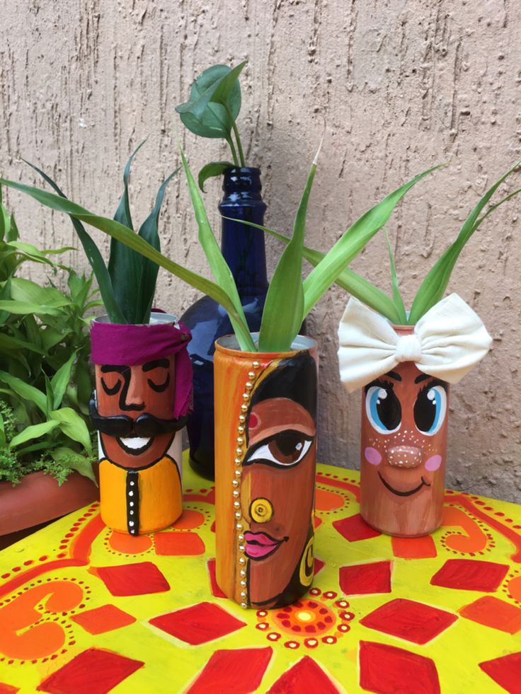 three vases with faces painted on them sitting on a table next to potted plants