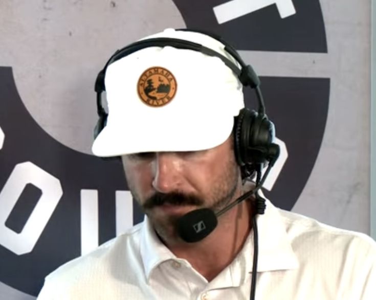 a man wearing a white hat and headphones in front of a wall with a logo on it