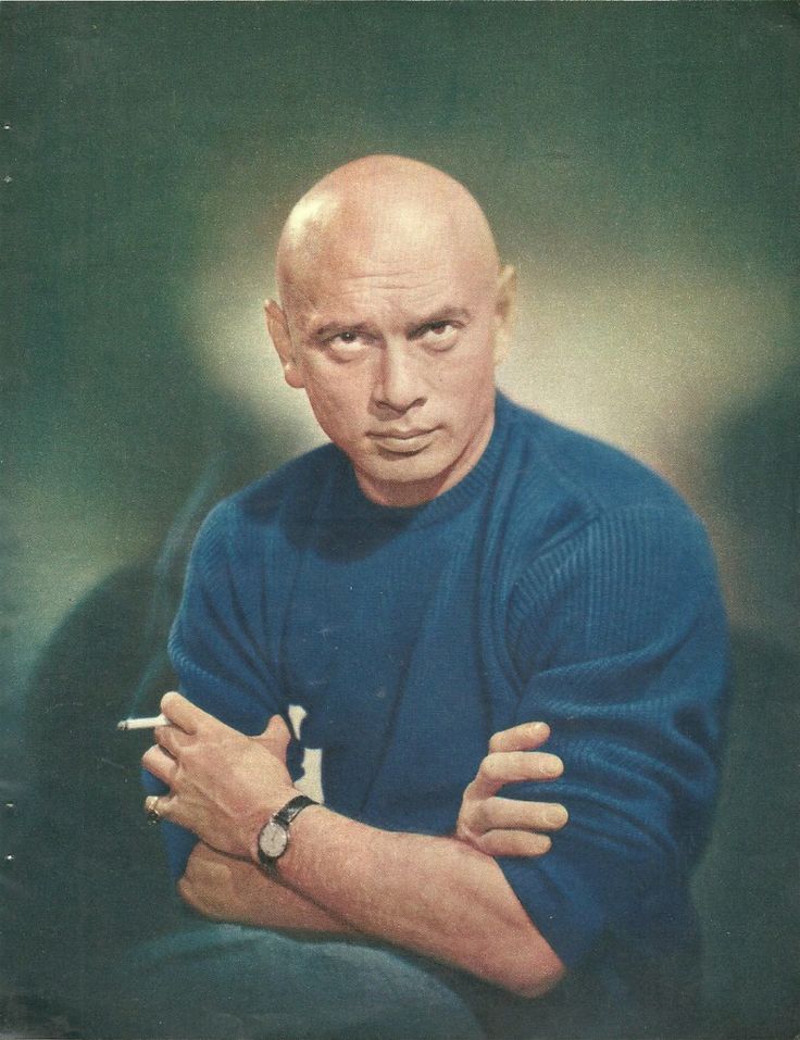 an old photo of a man with his arms crossed and looking at the camera while wearing a blue sweater