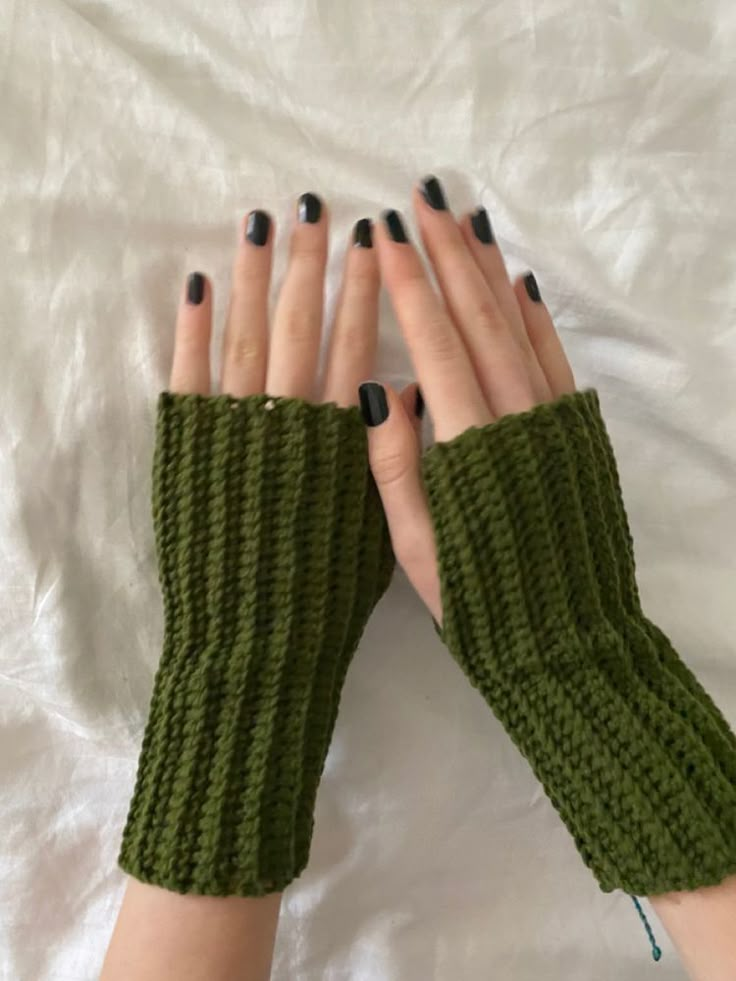 a woman's hands with black nails and green knitted arm warmers on top of a white sheet