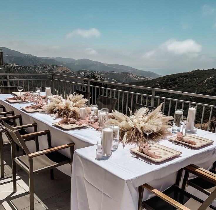 a long table with place settings on top of a balcony overlooking the ocean and mountains