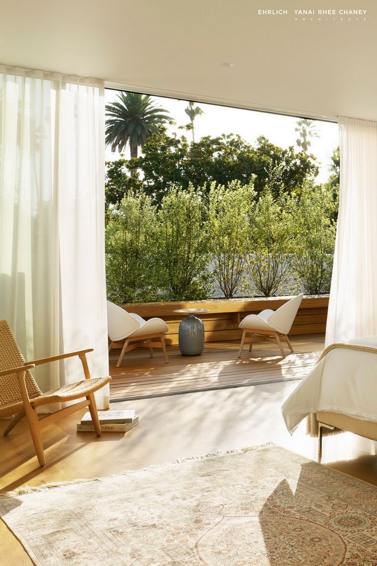 a bedroom with white drapes and curtains on the window sill, overlooking trees