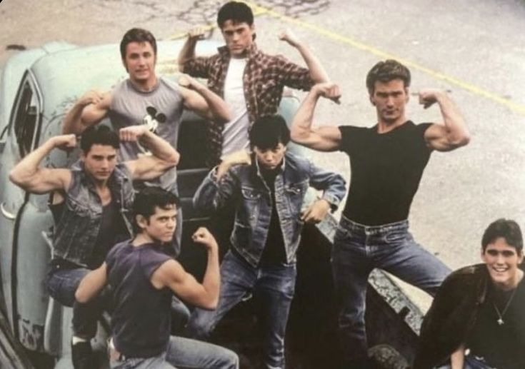 a group of young men posing in front of an old car