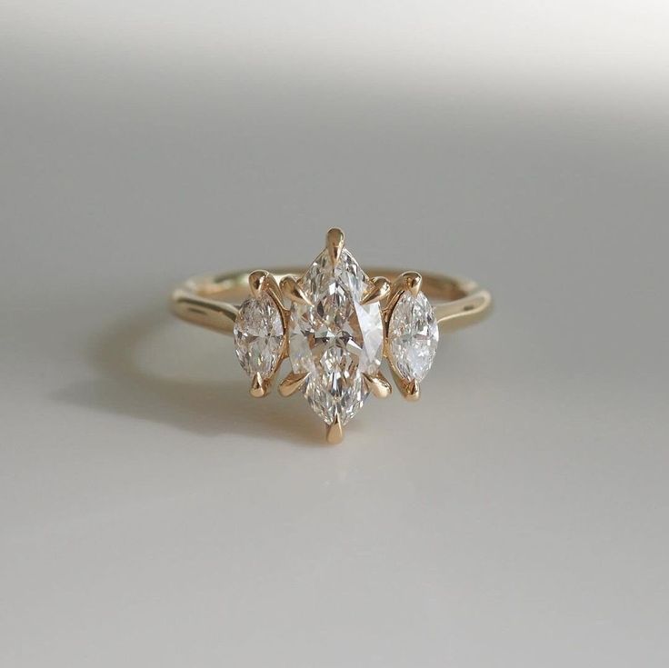 a three stone diamond ring sitting on top of a white surface with the center setting in yellow gold