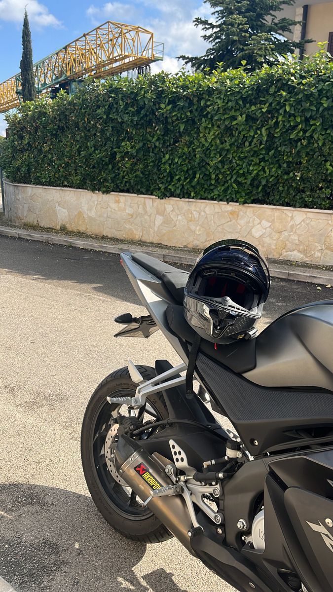 a black motorcycle parked on the street next to some bushes and trees with a roller coaster in the background