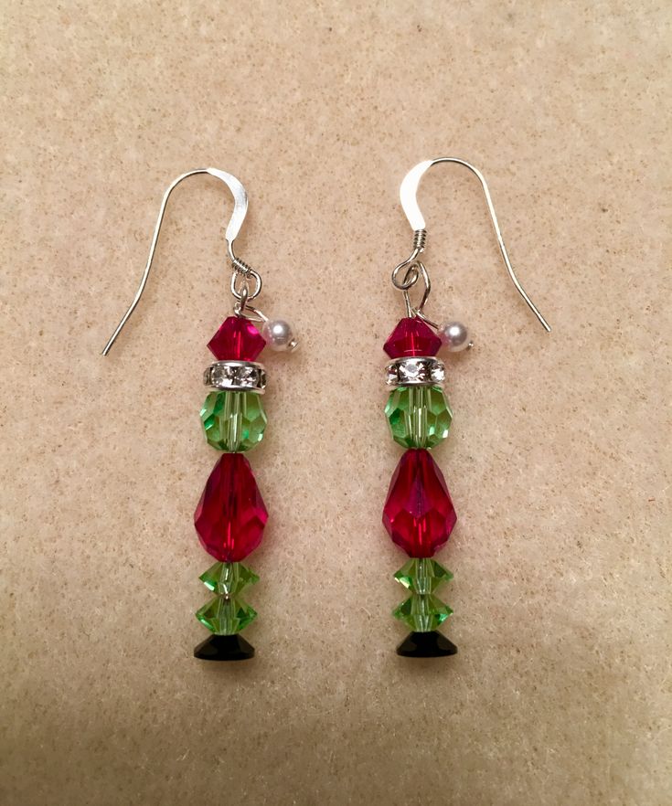 pair of red and green crystal earrings with silver earwires on beige carpeted surface