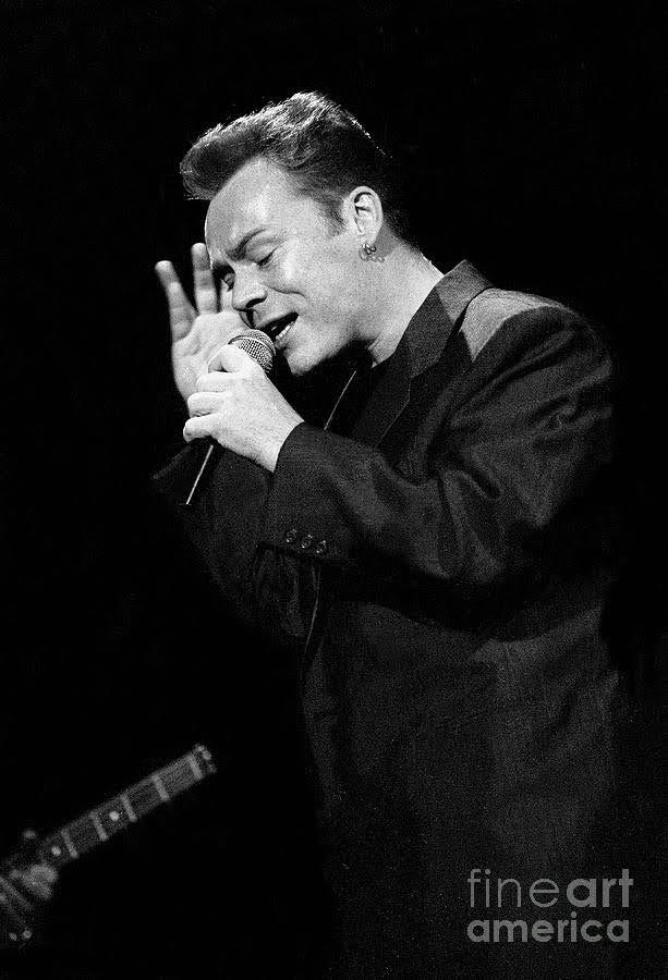 a black and white photo of a man holding his hand up in the air while singing