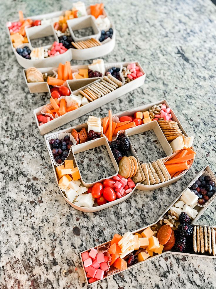 several trays filled with fruit and crackers on top of a marble countertop