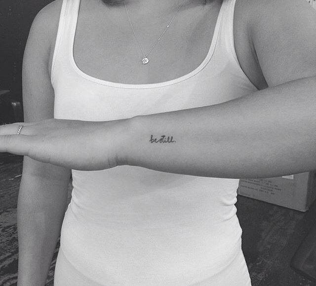 a woman with a tattoo on her arm pointing to the side and saying be still