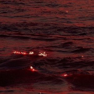 the sun is setting over the ocean with red light coming from it's lights