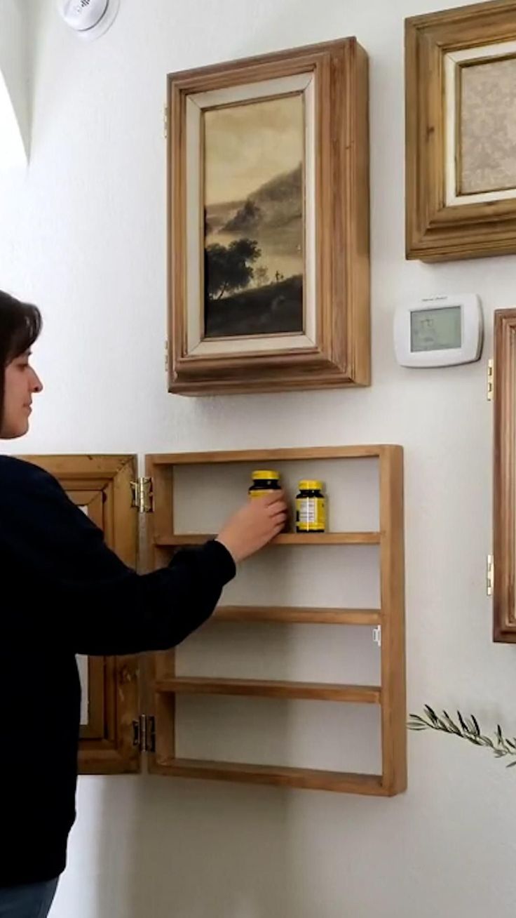 a woman is painting on the wall with paint rollers and she has two framed pictures above her