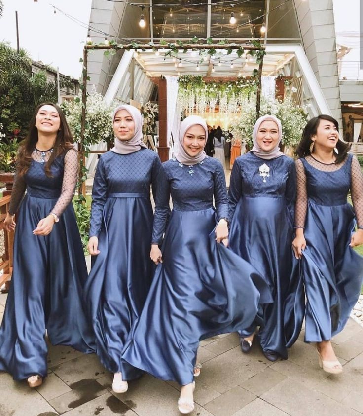 four women in long blue dresses are standing on the sidewalk and smiling at the camera