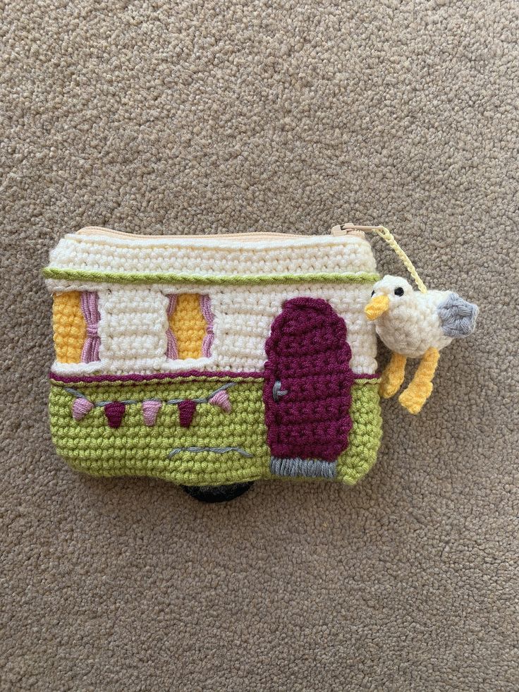 a crocheted purse with a bird on the handle and a house in the background