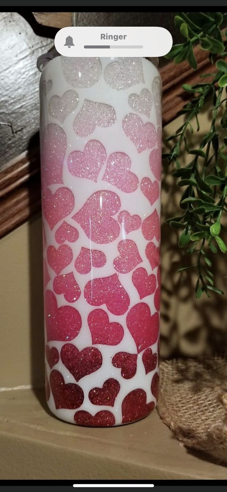 a pink and white candle with hearts on it sitting next to a potted plant