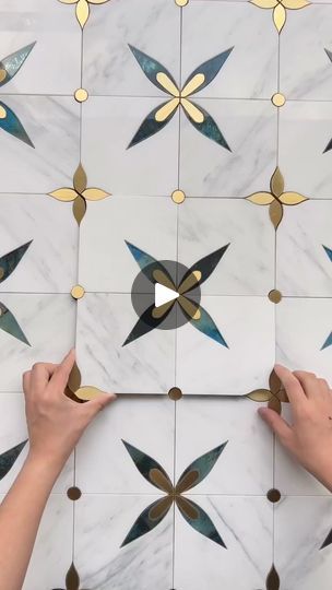 two hands are working on an artistic tile design with gold and silver circles in the center