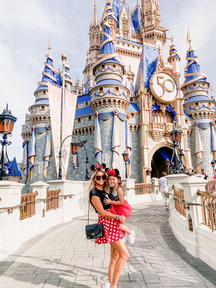 two women standing in front of a castle with minnie mouse ears on her head and one wearing a red polka dot dress