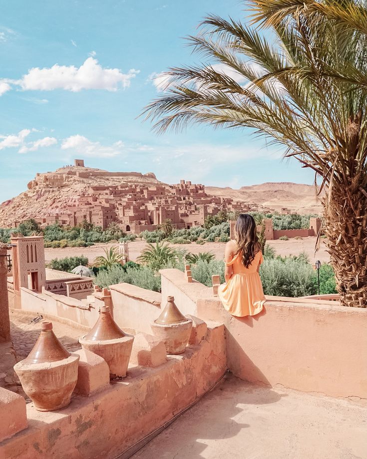 a woman standing on top of a roof next to a palm tree and building in the background