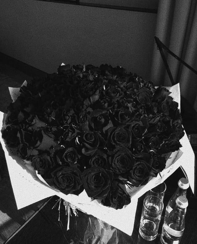 a large bouquet of black roses sits on a table next to two empty water bottles