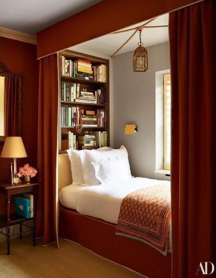 a bedroom with red curtains and a bed in the corner next to a bookshelf