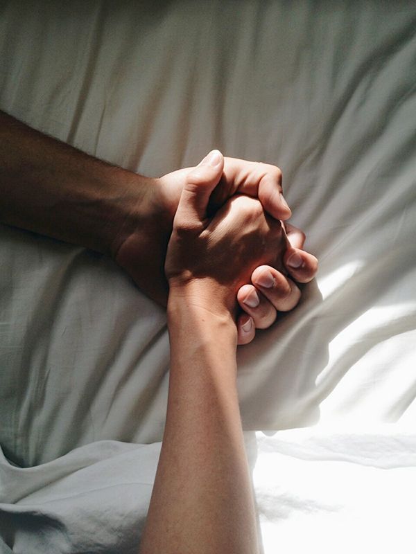 two people holding hands on top of a white sheet covered bed with sheets pulled back