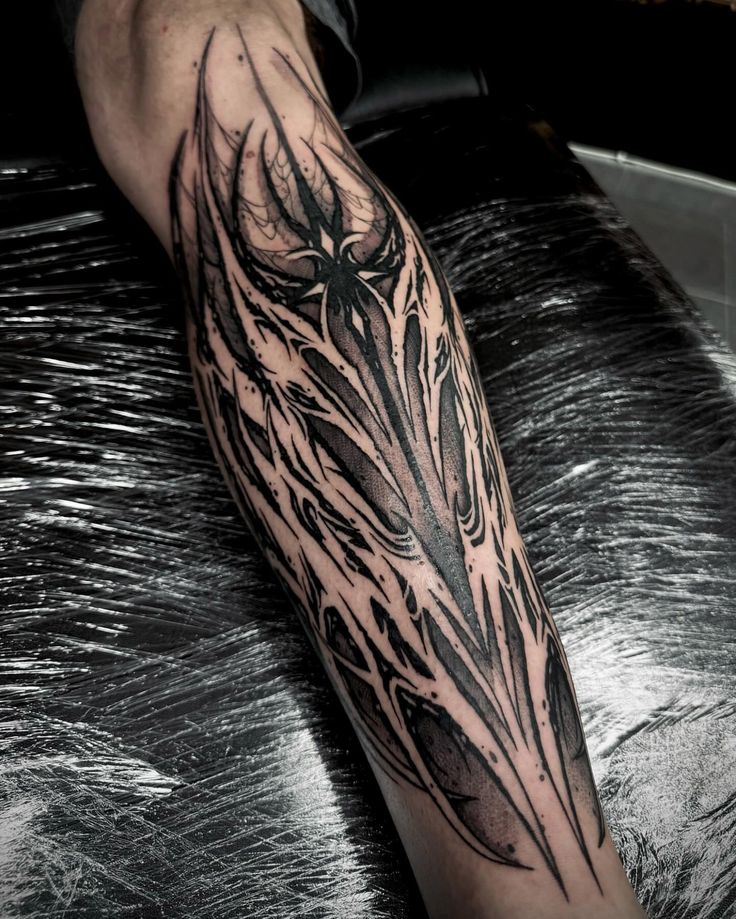 a man's arm with a black and grey tattoo design on the left forearm