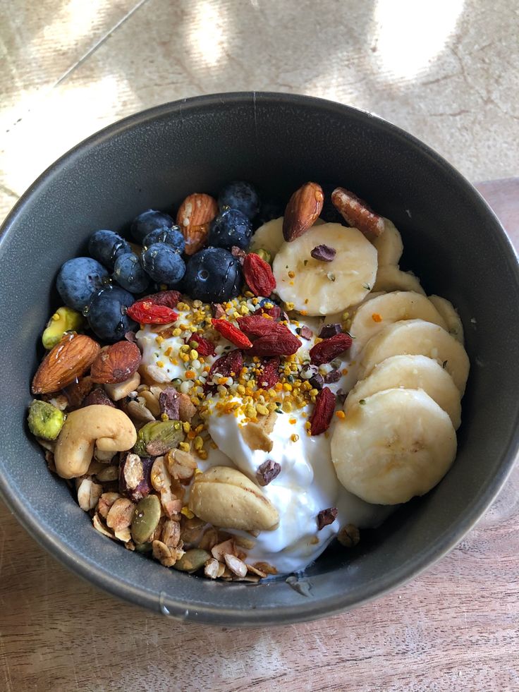 a bowl filled with yogurt, bananas, nuts and granola on top of a wooden table