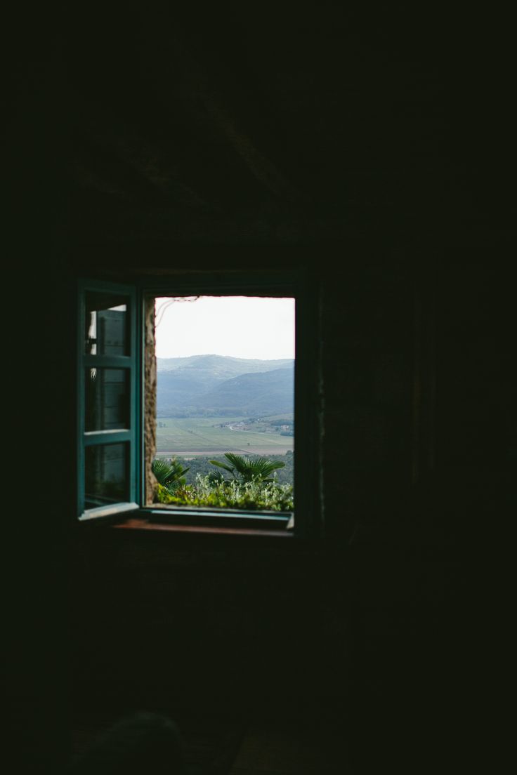 an open window in a dark room looking out at the countryside outside and hills beyond