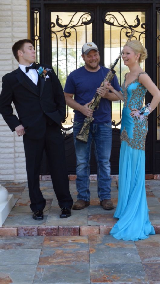 three people standing in front of a door, one holding a guitar and the other wearing a tuxedo