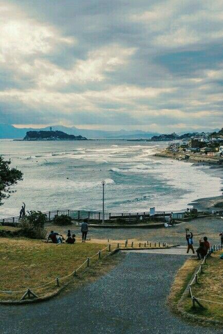 people are sitting on the grass by the water and walking up to the shore line