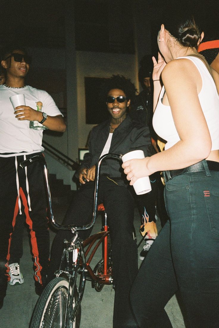 a woman riding a bike next to a man on a skateboard and another person standing behind her