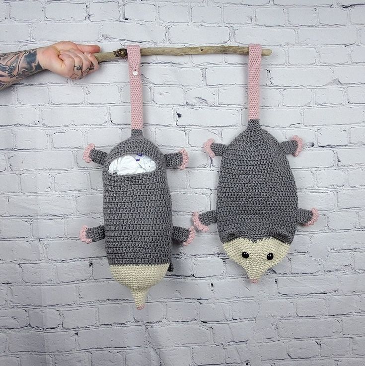 two crocheted stuffed animals hanging on a brick wall with a person's hand