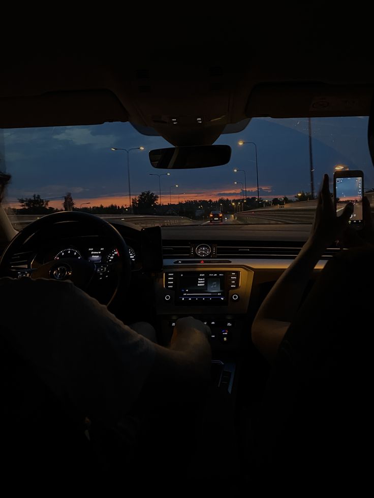 a person driving in the dark with their hands on the steering wheel and lights on