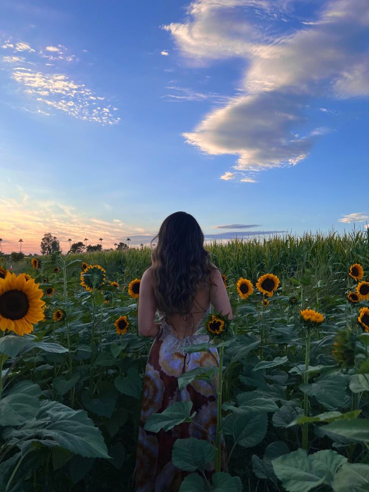 a woman standing in the middle of a field of sunflowers looking at the sky