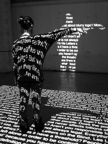 a person standing in front of a wall with words projected on it and pointing at the cross