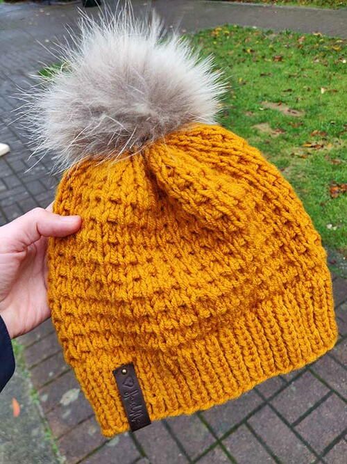 a person holding onto a yellow hat with a fur pom