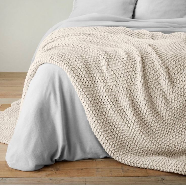 a bed covered in a white blanket and pillows on top of a wooden floor next to a window