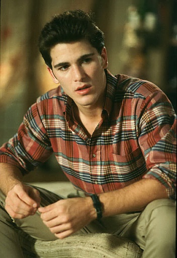 a man sitting on top of a couch wearing a plaid shirt and khaki pants